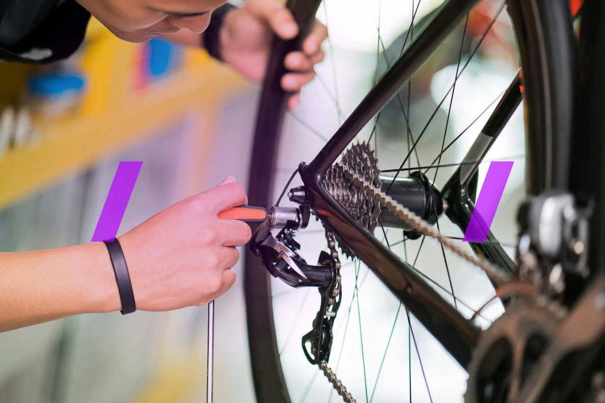The image shows a bicycle wheel, chain, and a mechanic who is making adjustments to the rear derailleur. The image represents an example rental equipment maintenance situation.