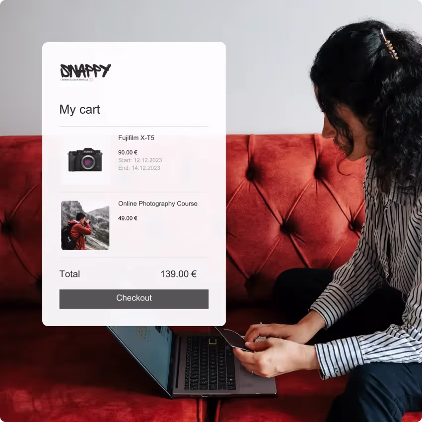 Person holding a credit card in front of an computer with an overlay of a shopping cart featuring digital camera