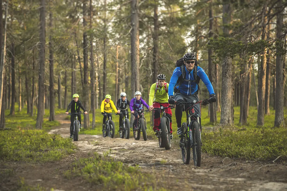 Äkäslompolo Sportshop customers riding rental bikes on a forest trail. Mountain and trail biking is popular activity in the Ylläs area.